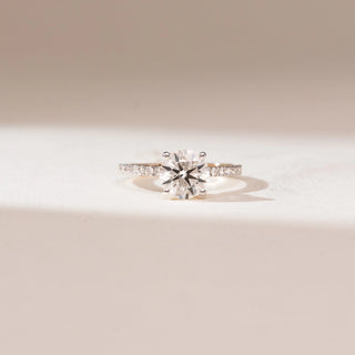 Front view of 14KT yellow gold ring featuring a round brilliant-cut centre diamond in a prong setting with a delicate pavé-set band of shimmering round diamonds.