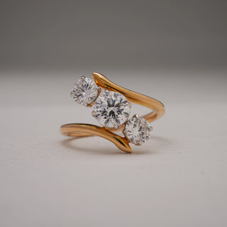 Front view of the Asymmetric Threefold Gold Diamond Ring crafted in hallmarked 18KT yellow gold. Features three round brilliant EF VVS diamonds in a staggered asymmetric design, centred by a 1.01-carat solitaire. The polished open band enhances the brilliance of the 1.9-carat total diamond weight, weighing 4.52 grams.