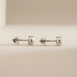 Side view of Cupid’s Love Diamond Stud Earrings on beige background. Crafted in 18KT hallmarked white gold with Bombay screw backs, featuring EF colour, VVS clarity lab grown diamonds weighing 2.05 carats total, including solitaire diamonds of 1.03 carats each.