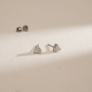 Angled view of Cupid’s Love Diamond Stud Earrings against soft beige background. Made in 18KT hallmarked white gold with Bombay screw closure. Set with EF VVS lab grown diamonds totaling 2.05 carats, solitaire 1.03 carats.