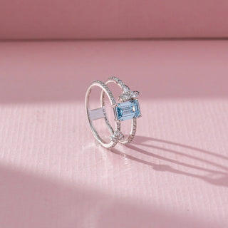 Side view of Emerald Cut Blue Stone Ring in 14KT White Gold, featuring a centred emerald-cut blue gemstone with lab grown diamond accents. Set on a pink backdrop, the design highlights depth and elegance.
