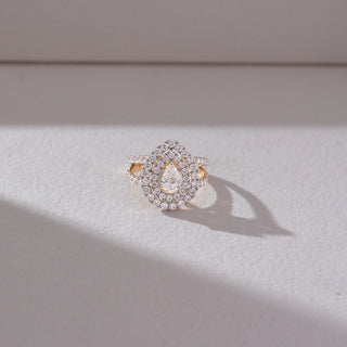 Top angled view of pear-shaped halo diamond ring in yellow gold, featuring a central lab-grown diamond with double halo layers. Set against a soft beige textured background with gentle shadows.