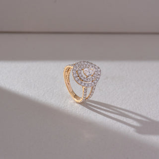 Side angled view of pear-shaped halo diamond ring in yellow gold, featuring a central lab-grown diamond with double halo layers and a split diamond-studded band, set against a soft beige background.