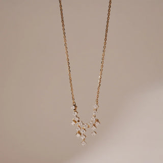 Delicate V-shaped Réia necklace adorned with small round lab grown diamonds clustered along a fine gold chain, styled against a soft neutral backdrop.
