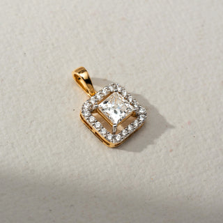 Top view of a gold square halo pendant featuring a princess-cut center Diamond surrounded by sparkling accent stones, displayed on a soft neutral surface in natural light.