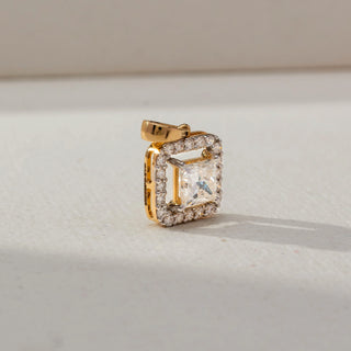 Side view of a gold square halo pendant featuring a princess-cut center Diamond surrounded by sparkling accent stones, displayed on a soft neutral surface in natural light.