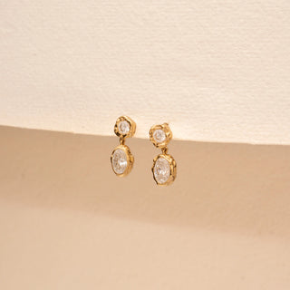 Angled view of 14KT Yellow Gold drop earrings with round and oval diamonds in organic bezel settings.