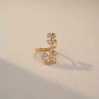 Side view of a floral wrap ring in 14 KT Yellow Gold, featuring star-shaped motifs set with round lab-grown diamonds along an elegant open-band design, displayed against a beige backdrop.