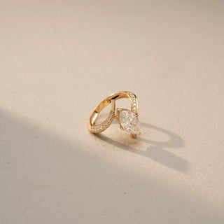 Side view of a marquise solitaire engagement ring in 14 KT Yellow Gold, featuring a marquise-cut lab-grown diamond embraced by a split pavé diamond band, displayed against a beige backdrop.