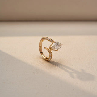 Angled view of a marquise solitaire engagement ring in 14 KT Yellow Gold, featuring a marquise-cut lab-grown diamond embraced by a split pavé diamond band, displayed against a beige backdrop.