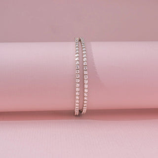 Front view of a 14KT white gold bracelet featuring round-cut diamonds, set against a pink background.
