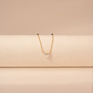 Close-up view of a 14KT yellow gold mangalsutra featuring a heart-cut diamond pendant with black beads, set against a beige background.