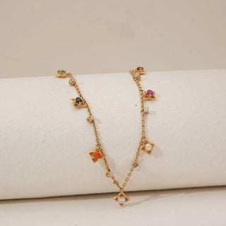 Front view of yellow gold multi-gem floral necklace featuring colourful gemstone flower charms and small diamond accents spaced along a delicate chain, displayed on a soft neutral jewellery stand.