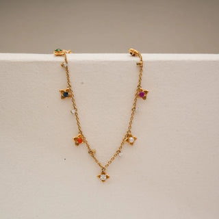 Front view of yellow gold multi-gem floral necklace with colourful gemstone flower charms and small diamond accents along a delicate chain, displayed on a neutral jewellery stand.