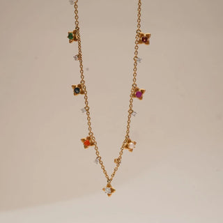 Close view of yellow gold multi-gem floral diamond necklace featuring colourful gemstone flower charms and tiny diamond accents spaced along a delicate chain against a soft neutral background.