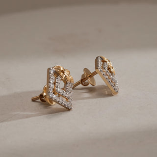 Side angle of Art Deco Statement Diamond Stud Earrings on beige background. Crafted in 14KT hallmarked yellow gold, with interlocked diamond-studded square frames and golden leaf motif. Set with EF colour, VVS clarity lab grown diamonds totaling 0.46 carats. Earrings weigh 2.913 grams with Bombay screw closure.