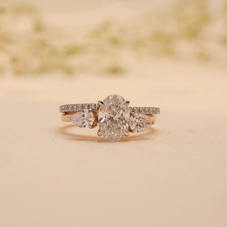 Front view of the Golden Harmony Diamond Bridal Set by Reia, highlighting the oval and pear-cut lab-grown diamonds on a pave gold band, set against a soft beige background.