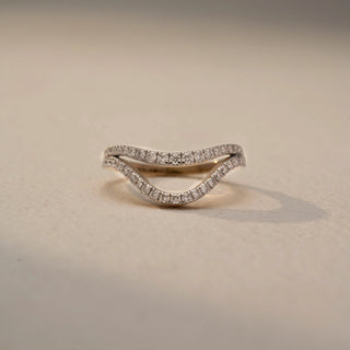 Front view of a curved diamond wedding band in White Gold, featuring pavé-set lab-grown diamonds along a graceful V-shaped silhouette, displayed against a beige backdrop.