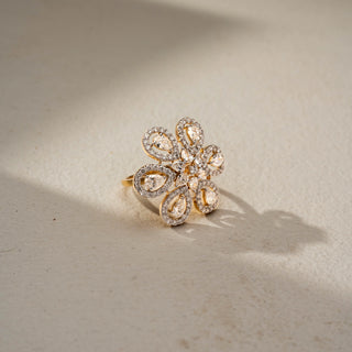 Angled view of a floral diamond statement ring in 14 KT Yellow Gold, featuring pear-shaped lab-grown diamonds framed by pavé-set halos in an intricate six-petal flower design, displayed against a beige backdrop.