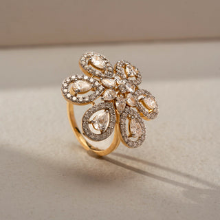 Close-up view of a floral diamond statement ring in 14 KT Yellow Gold, featuring pear-shaped lab-grown diamonds framed by pavé-set halos in an intricate six-petal flower design, displayed against a beige backdrop.