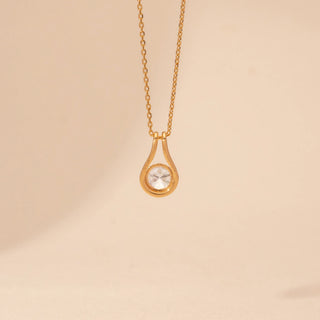 Close-up view of a 14KT yellow gold necklace featuring a round-cut diamond pendant, set against a beige background.