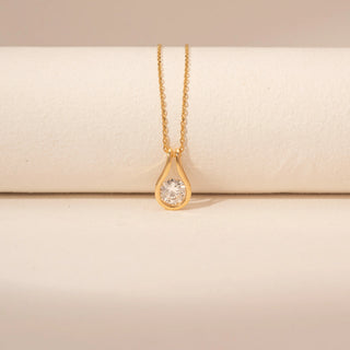 Front view of a 14KT yellow gold necklace featuring a round-cut diamond pendant, set against a beige background.