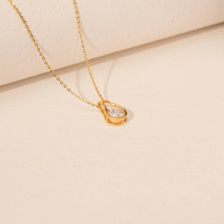 Angled view of a 14KT yellow gold necklace featuring a round-cut diamond pendant, set against a beige background.