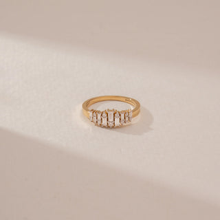 Close-up view of a diamond ring in 14KT Yellow Gold, featuring alternating baguette and round diamonds in a cluster setting against a beige backdrop.