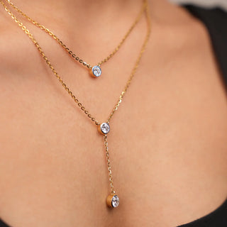 Lifestyle close-up of a Réia lab grown diamonds layered necklace in yellow gold, featuring bezel-set round-cut diamond charms arranged in a delicate drop design on the neckline.