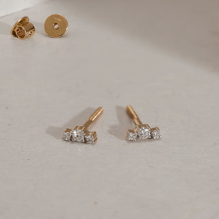 Close-up of Sleek Diamond Trio Studs in 14KT Yellow Gold on beige surface, showcasing three EF VVS round diamonds totalling 0.094 carats with screw-back closure for everyday wear.