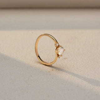 SIde view of a solitaire diamond ring in 14 KT Yellow Gold, featuring a round center diamond accented by tapered side diamonds on a sleek crossover band against a soft beige backdrop.