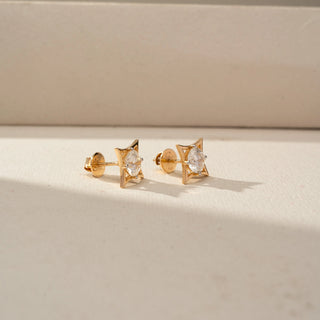 Side view of geometric diamond stud earrings in yellow gold, featuring round brilliant-cut diamonds set within sculptural openwork frames. Displayed on a beige backdrop, the profile highlights modern craftsmanship.