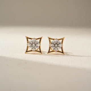 Front view of geometric diamond stud earrings in yellow gold, featuring round brilliant-cut diamonds set within sculptural openwork frames. Displayed on a beige backdrop, the design exudes modern elegance.