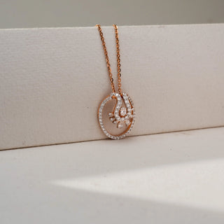 Close-up front view of a rose gold oval pendant necklace featuring a pavé-set diamond frame and an intricate floral-inspired diamond motif, displayed against a soft neutral backdrop.