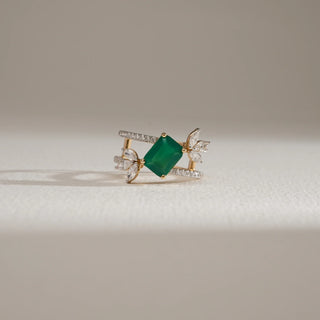 Front view of the Emerald Bloom Luxury Diamond Ring in 14KT Yellow Gold, featuring a vibrant emerald-cut green gemstone at the center, flanked by marquise and round diamond floral accents on a double diamond-studded band, placed against a soft light background.