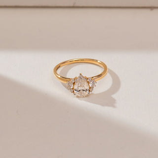 Top view of 14KT yellow gold ring featuring a pear-shaped centre diamond surrounded by round diamond cluster accents in a radiant sunburst design on a polished band.