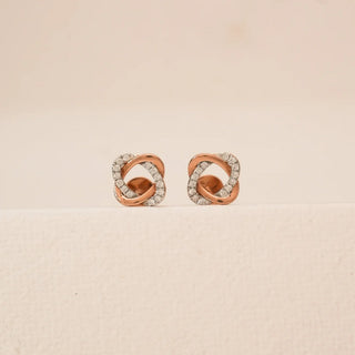 Front view of rose gold knotted diamond stud earrings featuring interlaced loop design accented with pavé-set round lab-grown diamonds, displayed on a neutral studio surface.