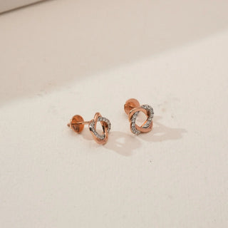 Angled view of rose gold knotted diamond stud earrings with interlocking loop design and pavé-set round lab-grown diamonds, placed on a soft neutral studio surface.