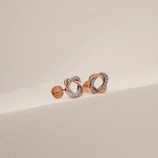 Close angled view of rose gold knotted diamond stud earrings featuring interlocking loops accented with pavé-set round lab-grown diamonds, displayed on a neutral studio surface.