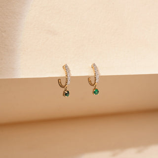 Side view of round lab-grown diamond drop earrings in 14 KT rose gold, featuring diamond huggie hoops with round emerald drop charms in a timeless elegant design