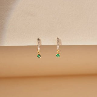 Front view of round lab-grown diamond drop earrings in 14 KT yellow gold, featuring diamond huggie hoops with round emerald drop charms in a timeless elegant design
