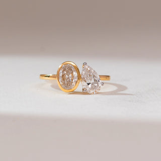 Front view of 14KT yellow gold ring featuring an oval-cut diamond in a bezel setting paired with a pear-shaped diamond in a prong setting on a sleek polished band.