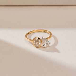 Top view of 14KT yellow gold open ring featuring an oval-cut diamond in a bezel setting and a pear-shaped diamond in a prong setting on a sleek polished band.