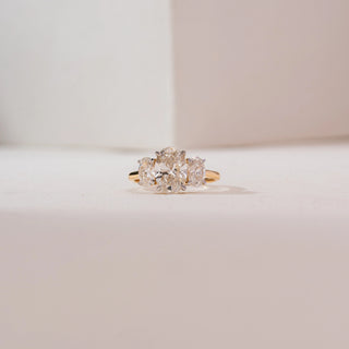 Front view of a 14KT yellow gold triple oval solitaire diamond ring featuring three prong-set oval diamonds in a row on a sleek polished band, displayed on a soft neutral background.
