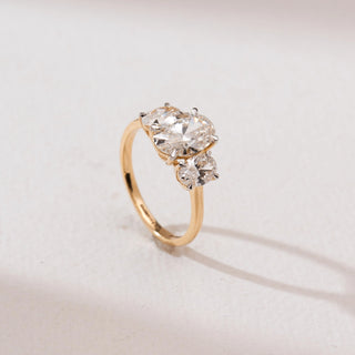 Side angle view of a 14KT yellow gold triple oval solitaire diamond ring with three prong-set oval diamonds in a row on a sleek polished band, set against a soft neutral background.