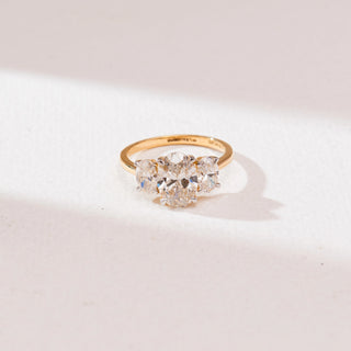 Top view of a 14KT yellow gold triple oval solitaire diamond ring featuring three prong-set oval diamonds aligned in a row on a sleek polished band, displayed on a soft neutral surface.