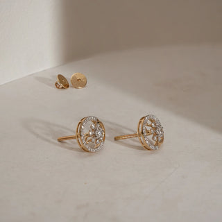 Floral diamond stud earrings in 14KT Yellow Gold with a central floral cluster framed by a round diamond halo, displayed on a beige surface with detached Bombay screw backs.