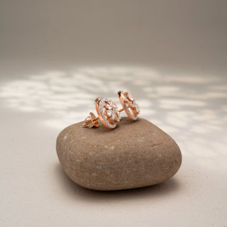 Side view of floral diamond stud earrings in 14 KT Rose Gold, featuring marquise-cut diamond petals within pavé-set circular frames, displayed on a textured stone surface.
