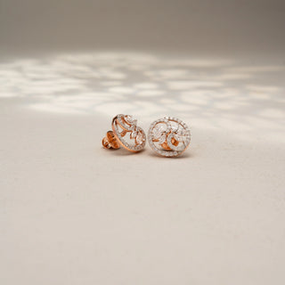 Angled view of floral diamond stud earrings in 14 KT Rose Gold, featuring marquise-cut diamond petals within pavé-set circular frames, displayed on a textured stone surface.
