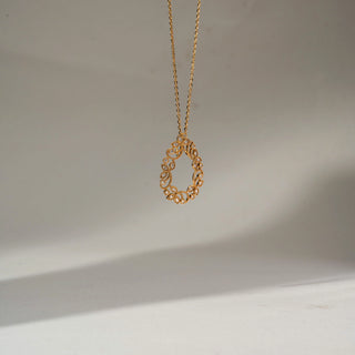 Side view of a delicate gold teardrop pendant necklace with intricate floral filigree and sparkling stone accents, suspended on a fine chain against a soft neutral background.